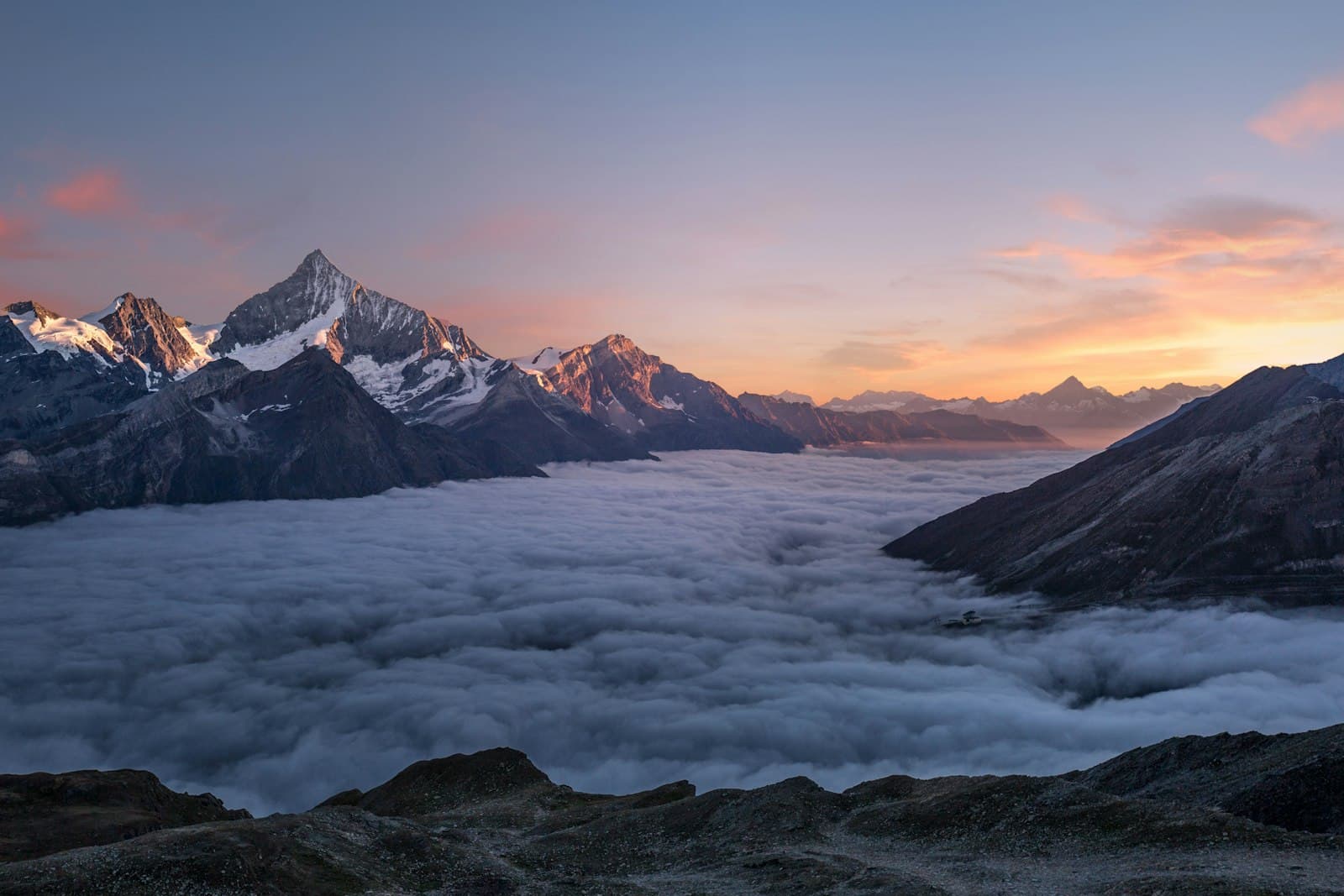 Snow-capped peaks rising above a sea of clouds at sunrise