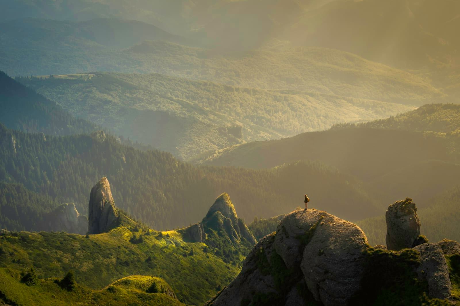 Lone hiker standing on a rock above a sunlit green valley