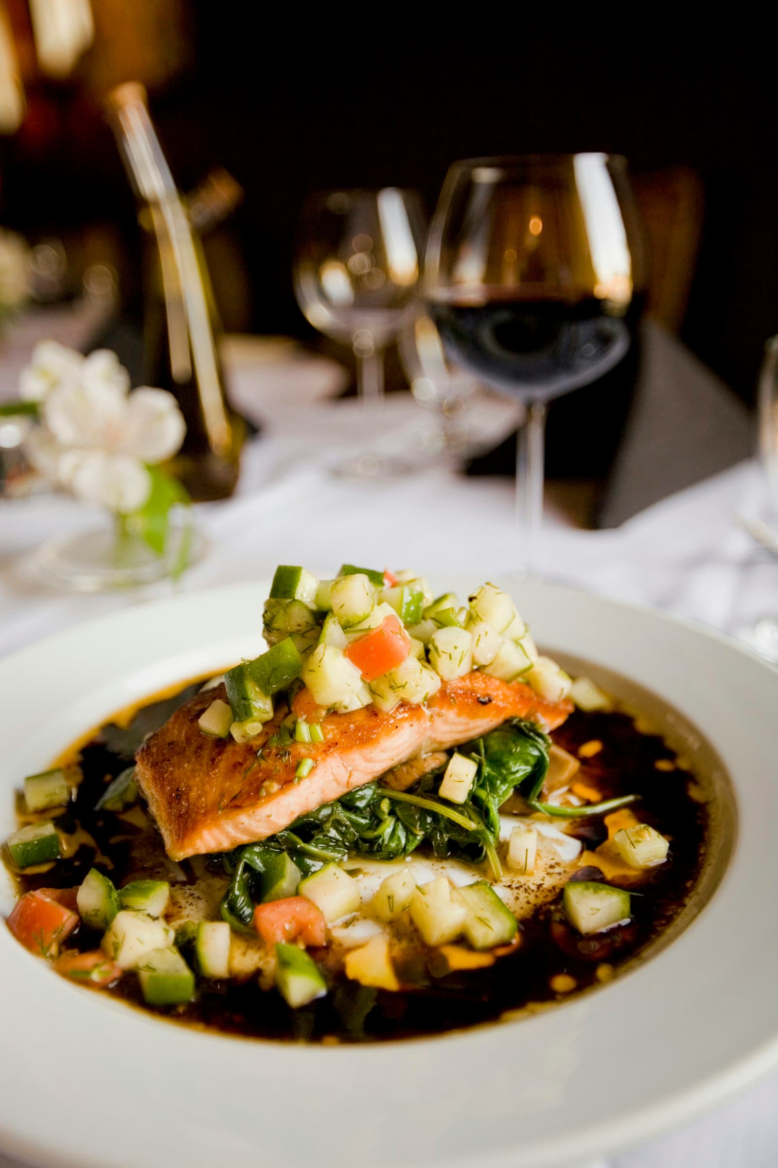Roasted salmon plated with greens and a dark reduction, red wine behind